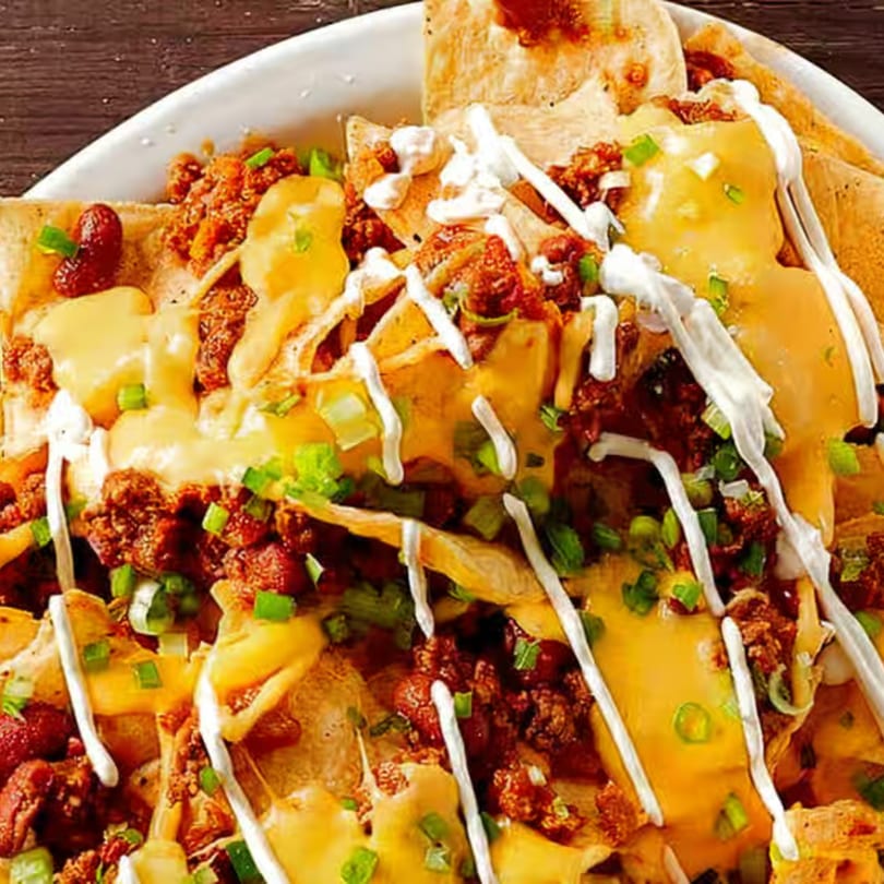 Close-up of Mexican nachos with melted cheese, ground meat, sour cream, and green onions.