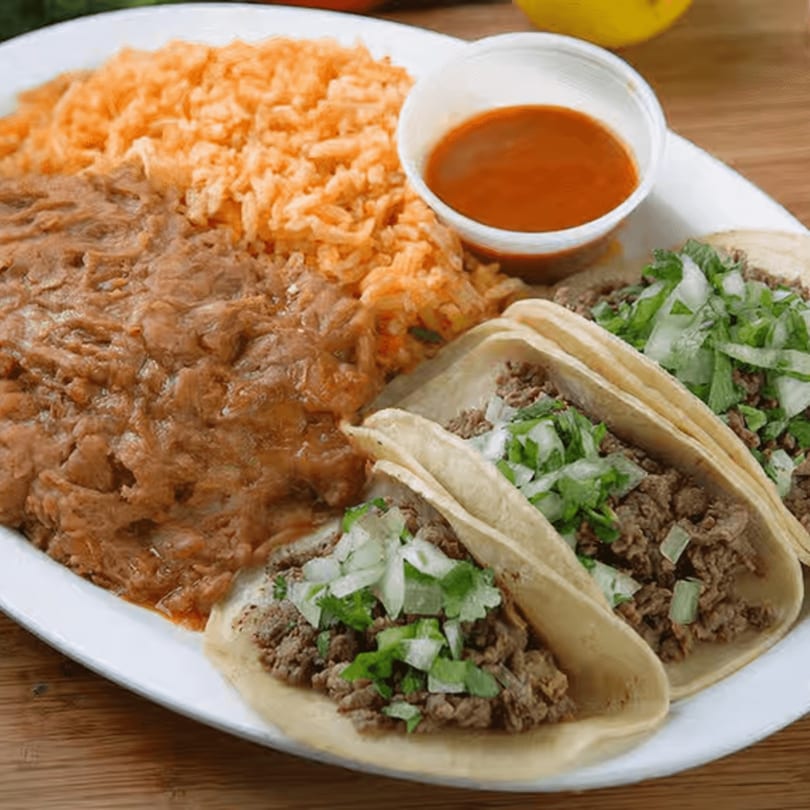 Three beef tacos with onions and cilantro, served with rice, refried beans, and red sauce.