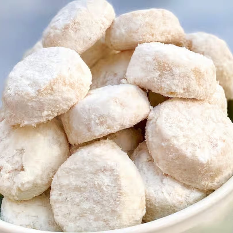 A close-up of a bowl filled with Mexican wedding cookies, coated in powdered sugar.