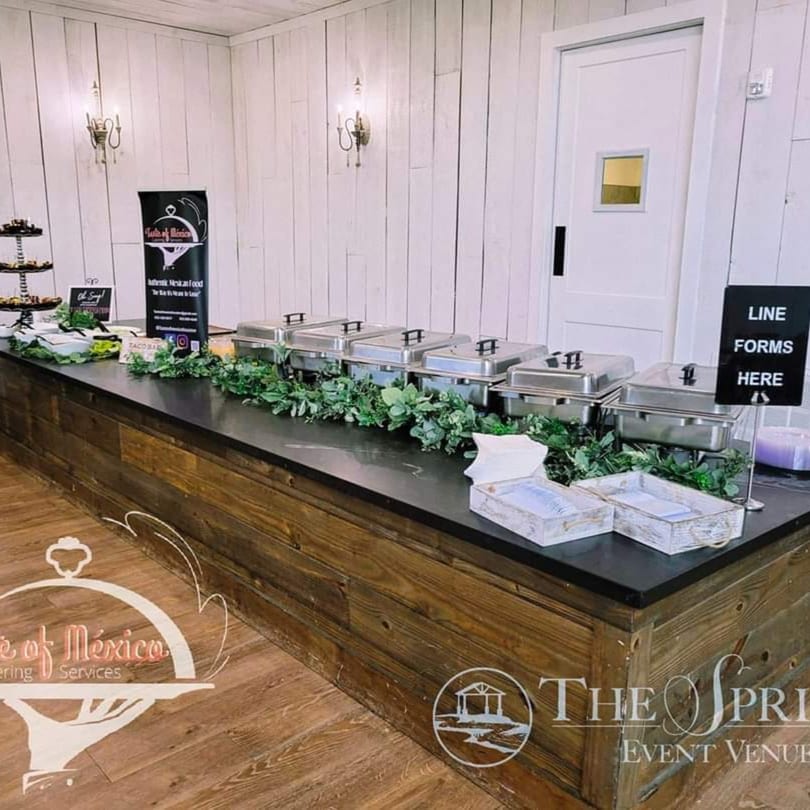 A Taste of Mexico catering buffet with chafing dishes, greenery, and a "Line Forms Here" sign.