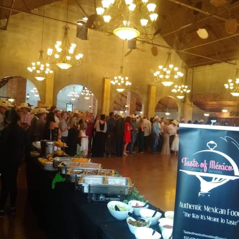 A Taste of Mexico catering buffet with chafing dishes and toppings, and guests mingling in a large hall.