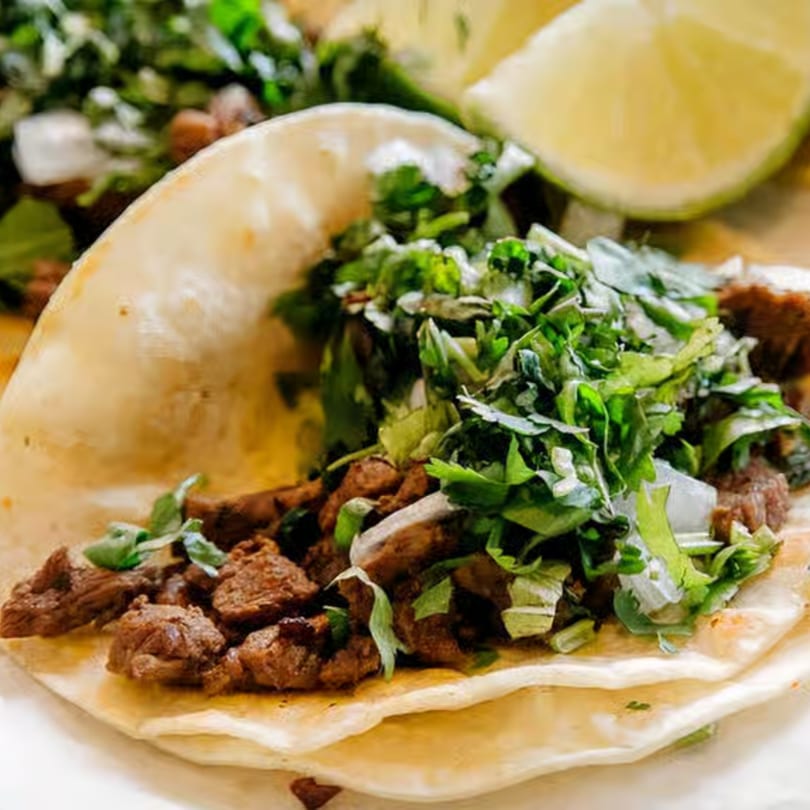 Close-up of a Mexican taco with meat, cilantro, onions, and a lime wedge.