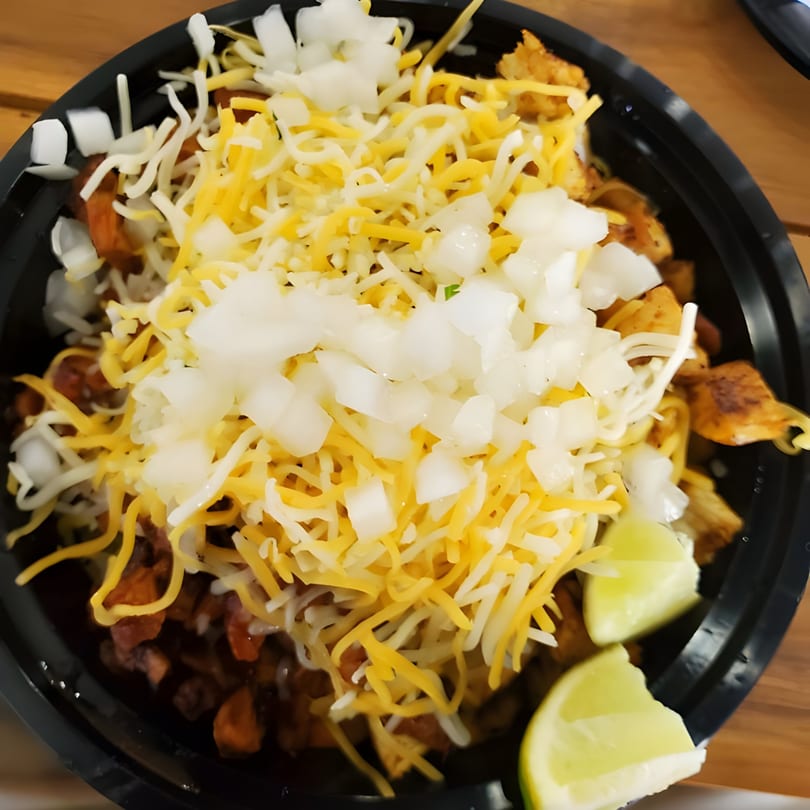 Mexican dish with shredded cheese, diced onions, and lime wedges in a black bowl.