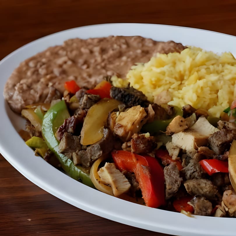 A Mexican fajita plate with steak, chicken, peppers, onions, rice, and refried beans.