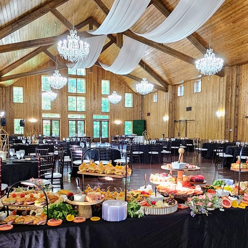 A spacious banquet hall with wooden walls, chandeliers, and tables laden with appetizers and desserts.