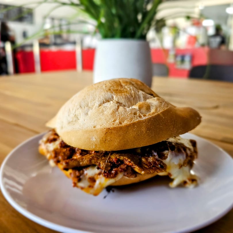 A Mexican torta sandwich with melted cheese and saucy meat on a white plate.