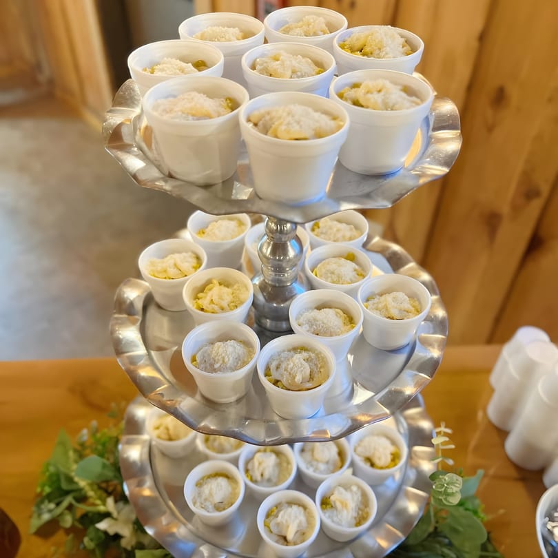 A three-tiered silver stand holds numerous small white cups filled with Mexican street corn, topped with cheese.