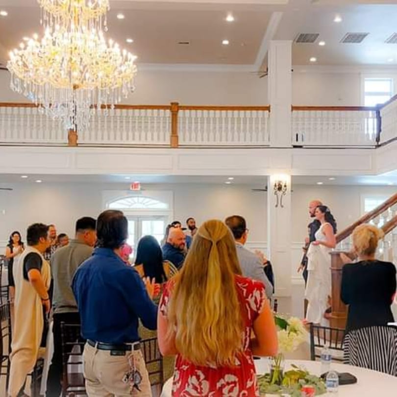 Guests gather in a spacious, elegant dining hall with a grand chandelier and balcony.